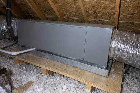 Closed sheet-metal air handler cabinet on a platform in an attic with a metal drain pan beneath it and a duct leaving one end