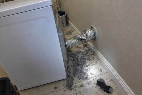 Dryer pulled away from a laundry room wall with a crushed foil duct behind it and lint on the floor