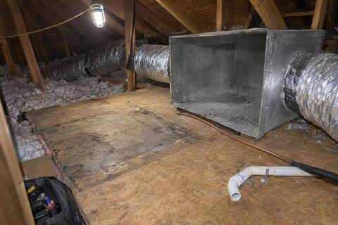 Empty platform in an attic where an air handler has been taken out, an open sheet-metal box with dust inside and flexible ducts still attached to it