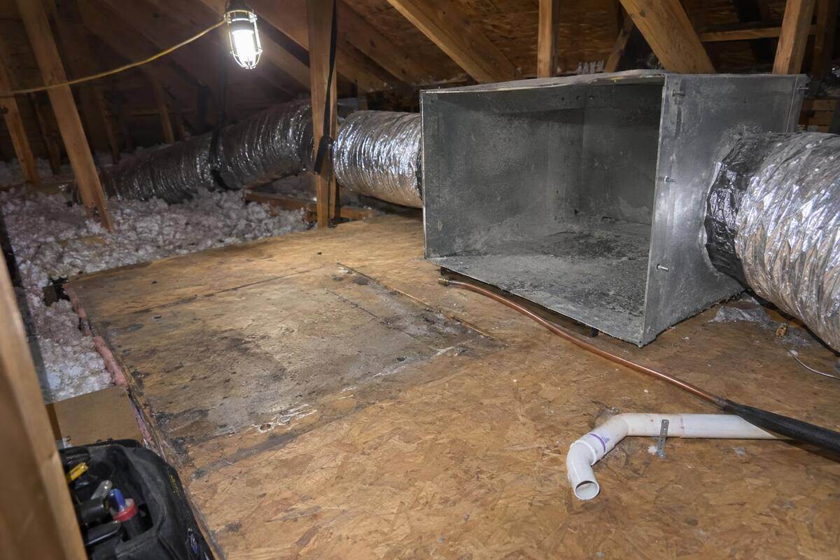 Empty platform in an attic where an air handler has been taken out, an open sheet-metal box with dust inside and flexible ducts still attached to it